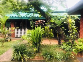 Un exuberante jardín con diversas plantas y una cerca blanca en enrejado frente a un edificio con techo verde.