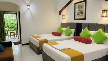 A hotel room with two beds, a sofa, a dining table, and a balcony with a view of greenery.