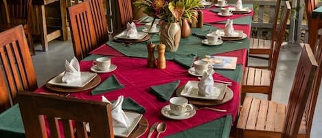A dining area with wooden tables and chairs, red tablecloths, and a bamboo backdrop.