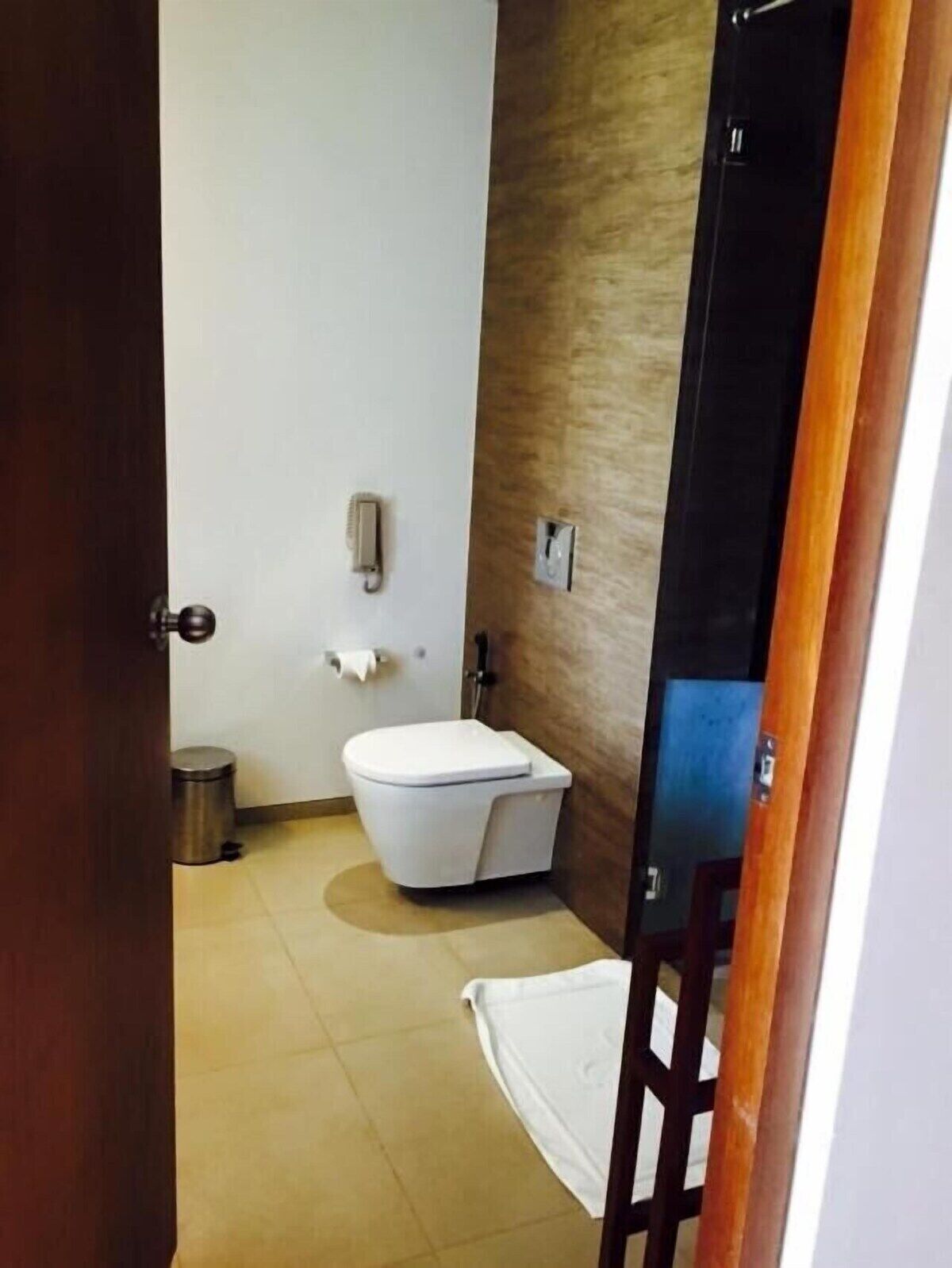 A small, clean bathroom with a white toilet, a trash can, and a towel on the floor.