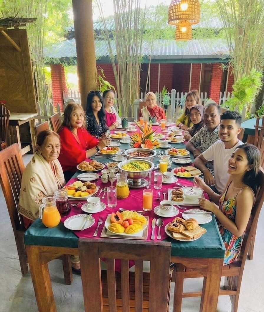 Un grupo de personas cenando en una mesa al aire libre, con diversos platos y bebidas.