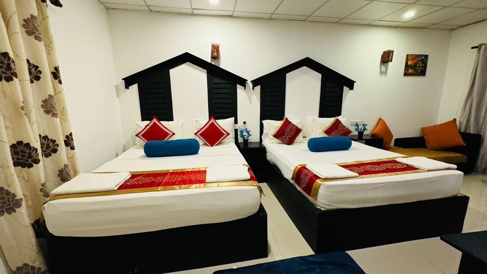 Une chambre d’hôtel avec deux lits, chacun doté d’une tête de lit noire, de draps blancs et de coussins décoratifs rouges.