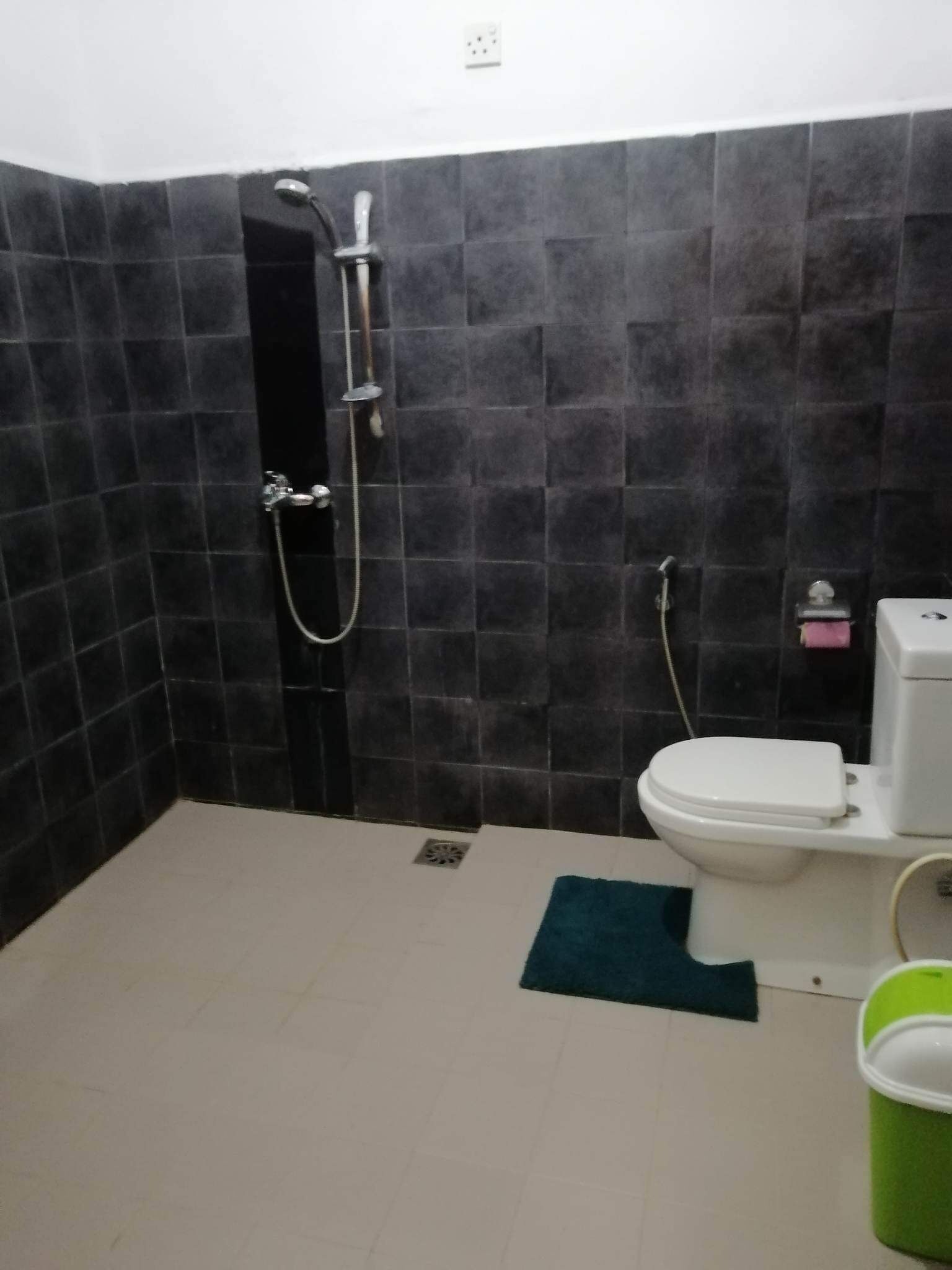 A small bathroom with a shower, toilet, and a green bucket.