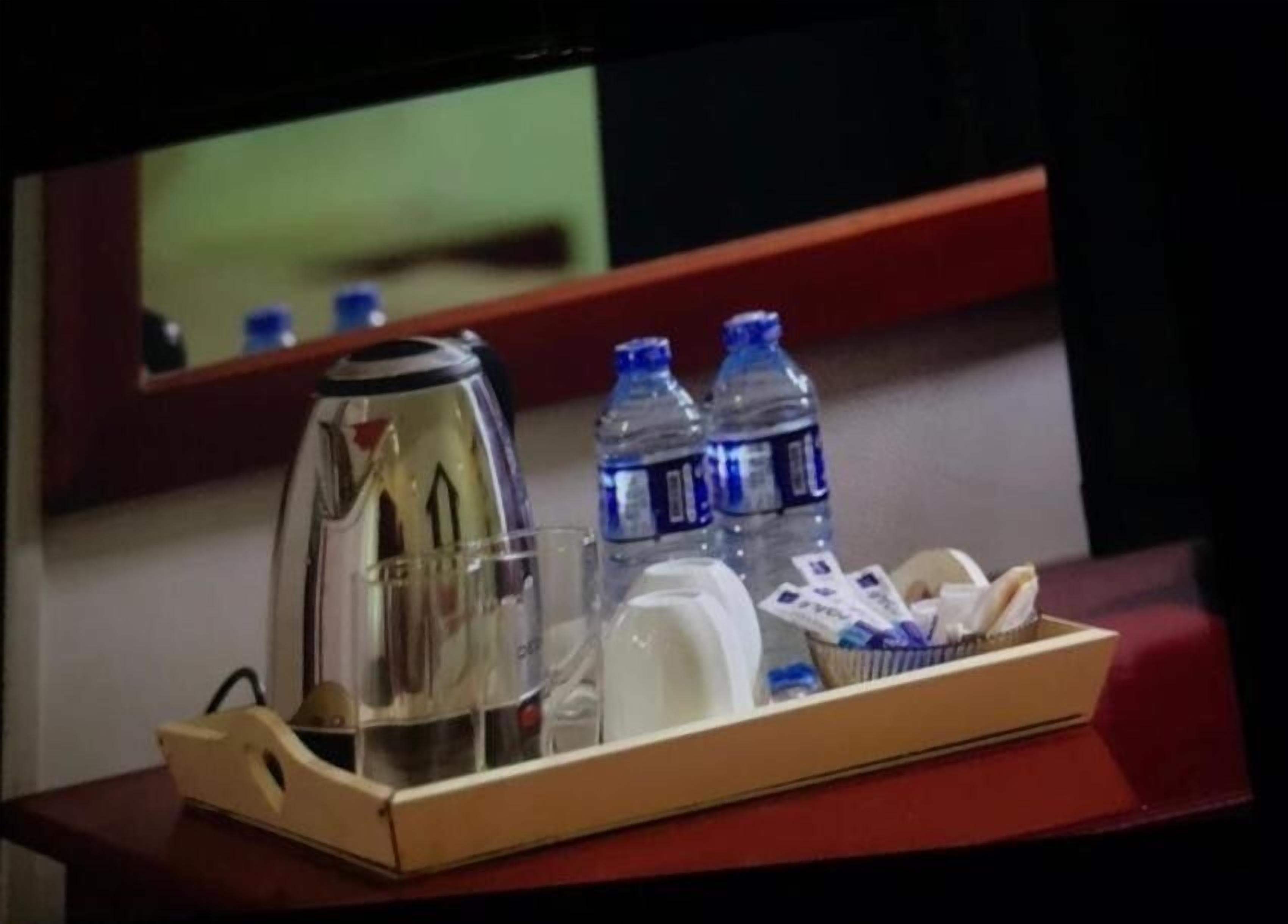 A tray with a coffee maker, two water bottles, a glass, and a tissue box on a wooden table.