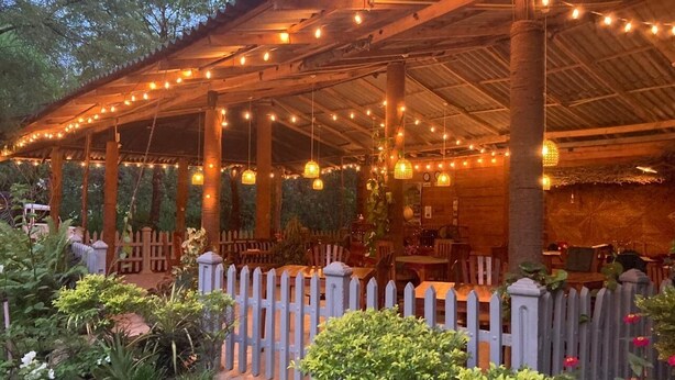 An outdoor patio with string lights, wooden columns, and a white picket fence.