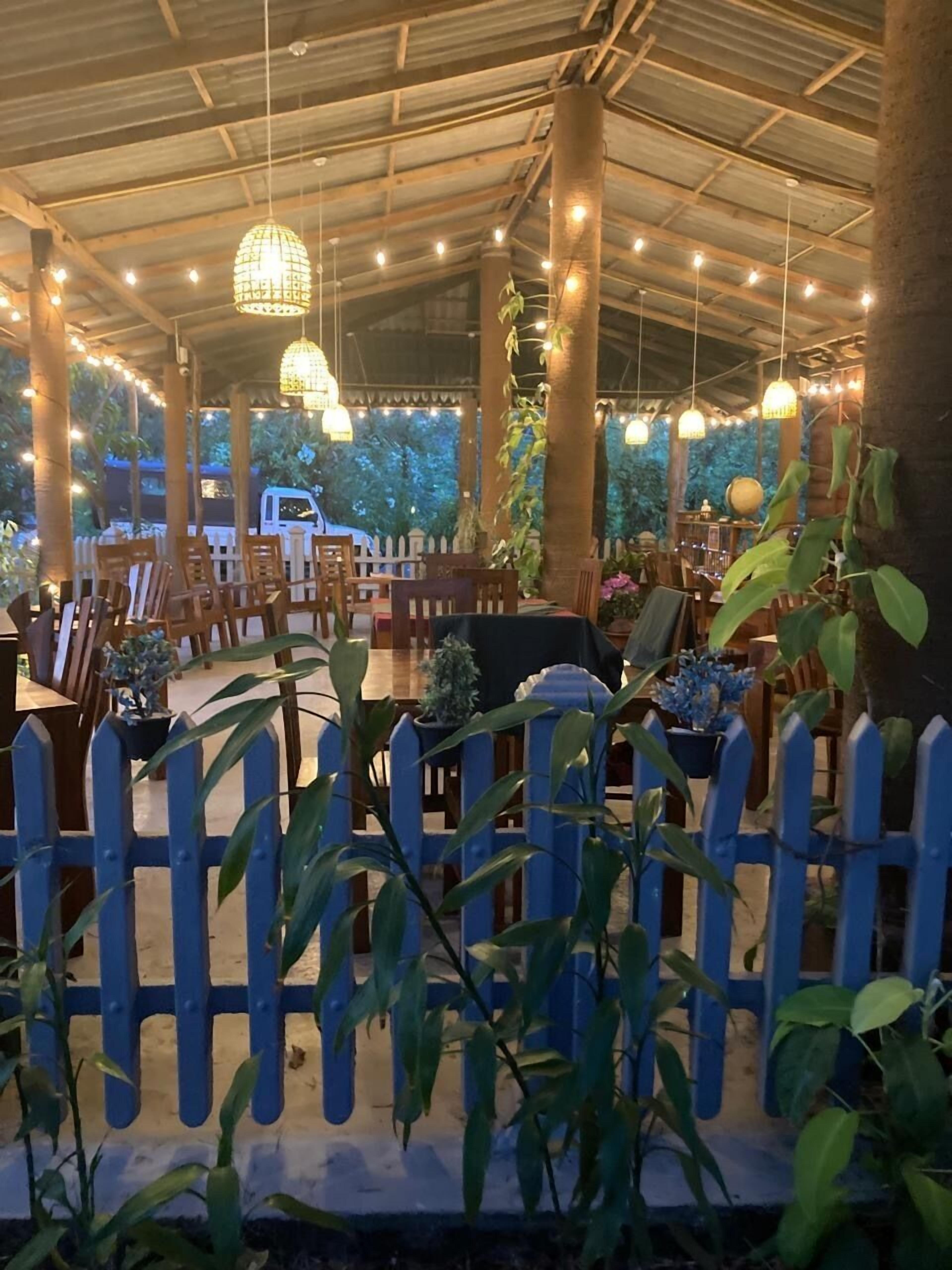 An outdoor dining area with tables and chairs, a blue picket fence, and hanging lights.