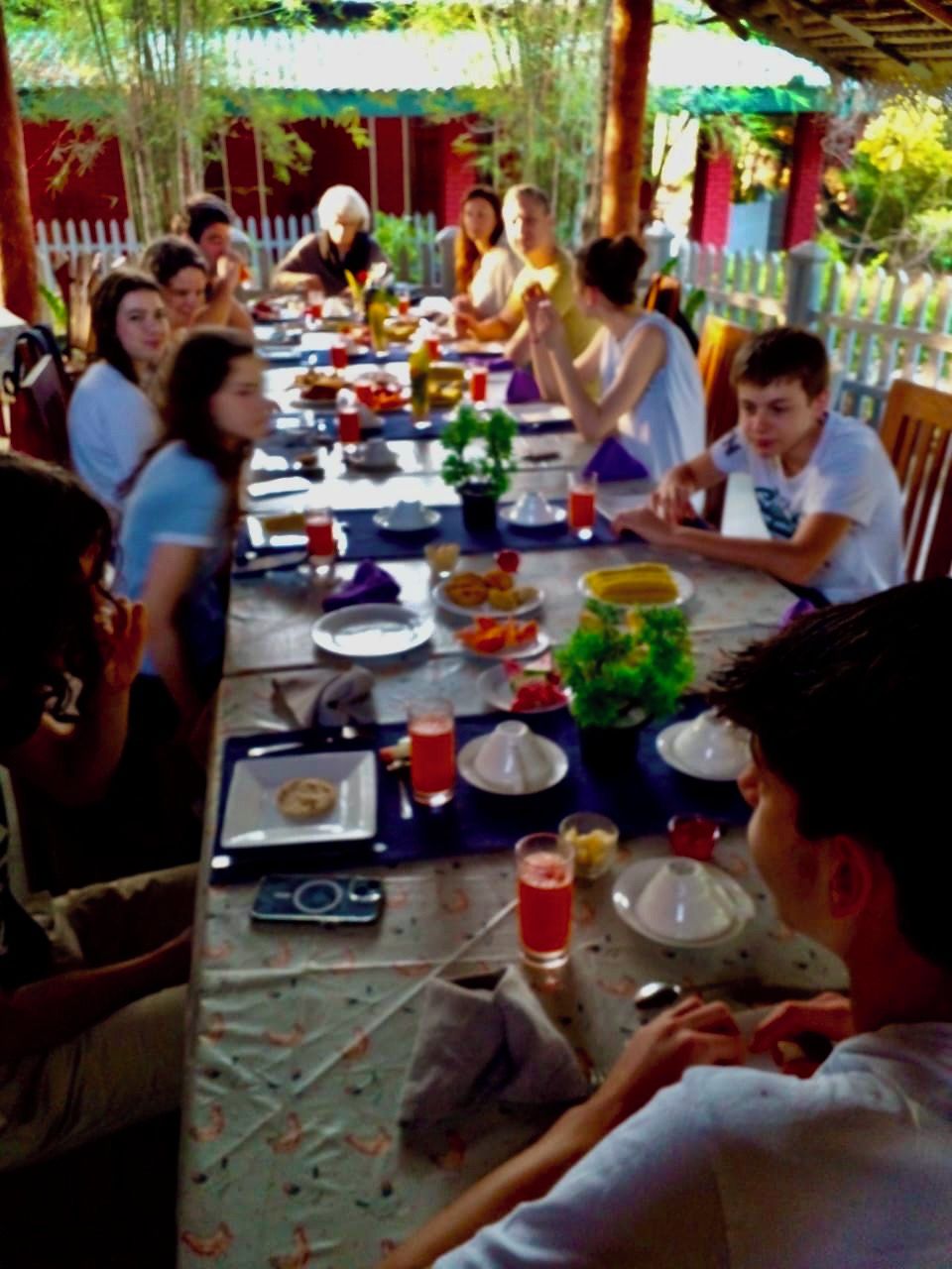 Un grupo de personas cenando en una mesa al aire libre con diferentes platos y bebidas.