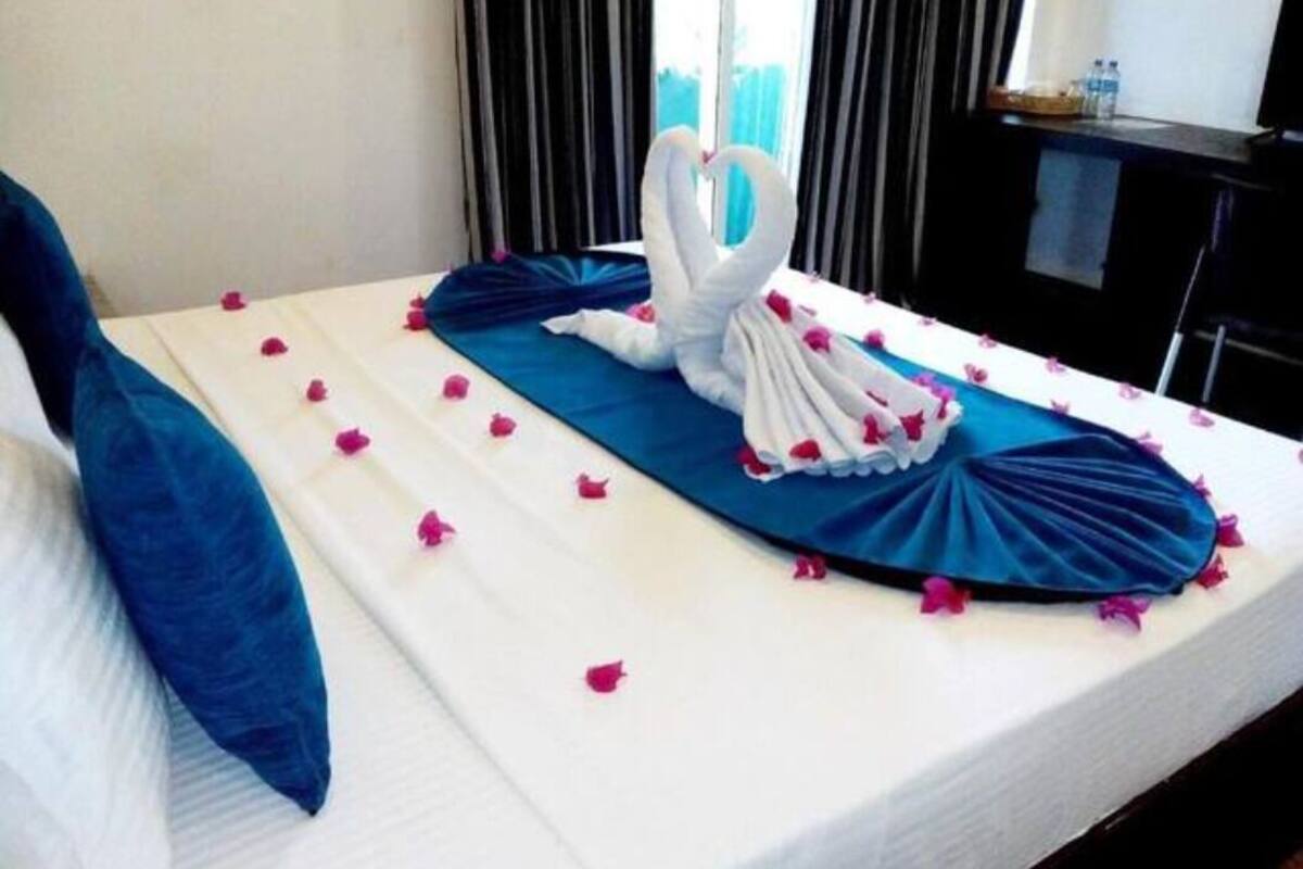 A bed with a blue bedspread, white pillows, and a heart-shaped towel arrangement.