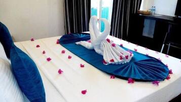 Una cama con colcha azul, almohadas blancas y una toalla dispuesta en forma de corazón.