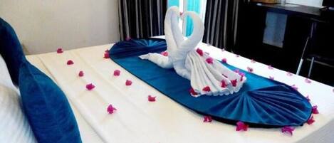 A bed with a blue bedspread, white pillows, and a heart-shaped towel arrangement.