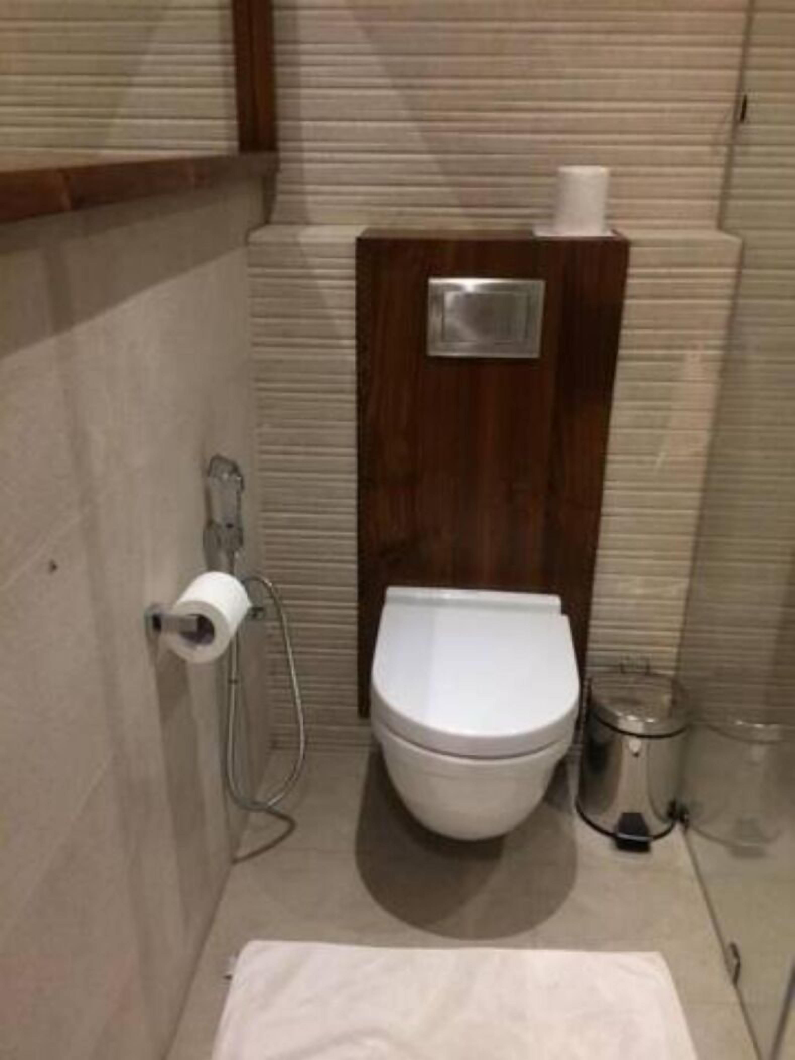 A small, compact bathroom with a white toilet, a wooden vanity, and a metal trash bin.