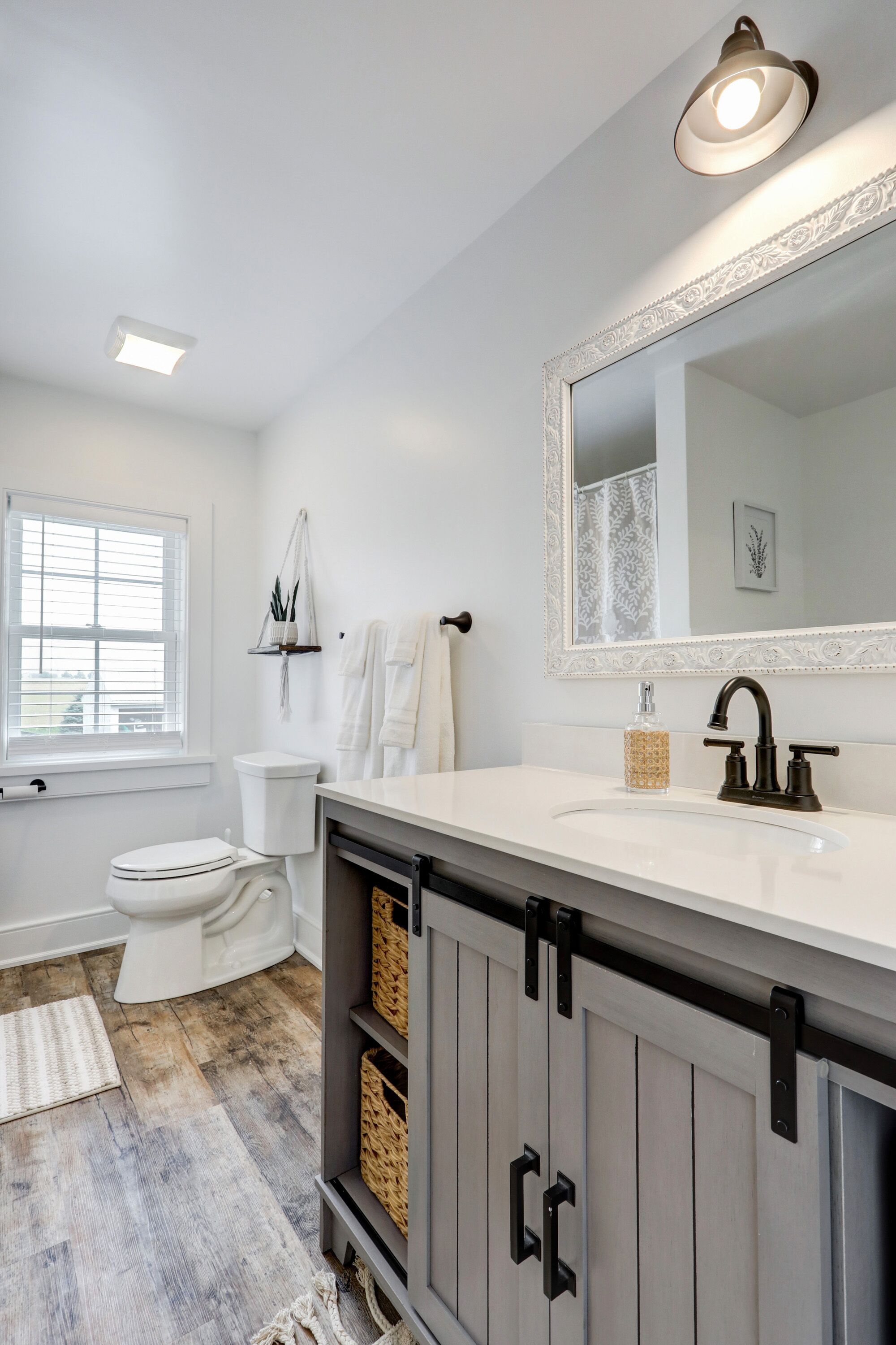 A bathroom with a white vanity, a large mirror, a toilet, and a window.