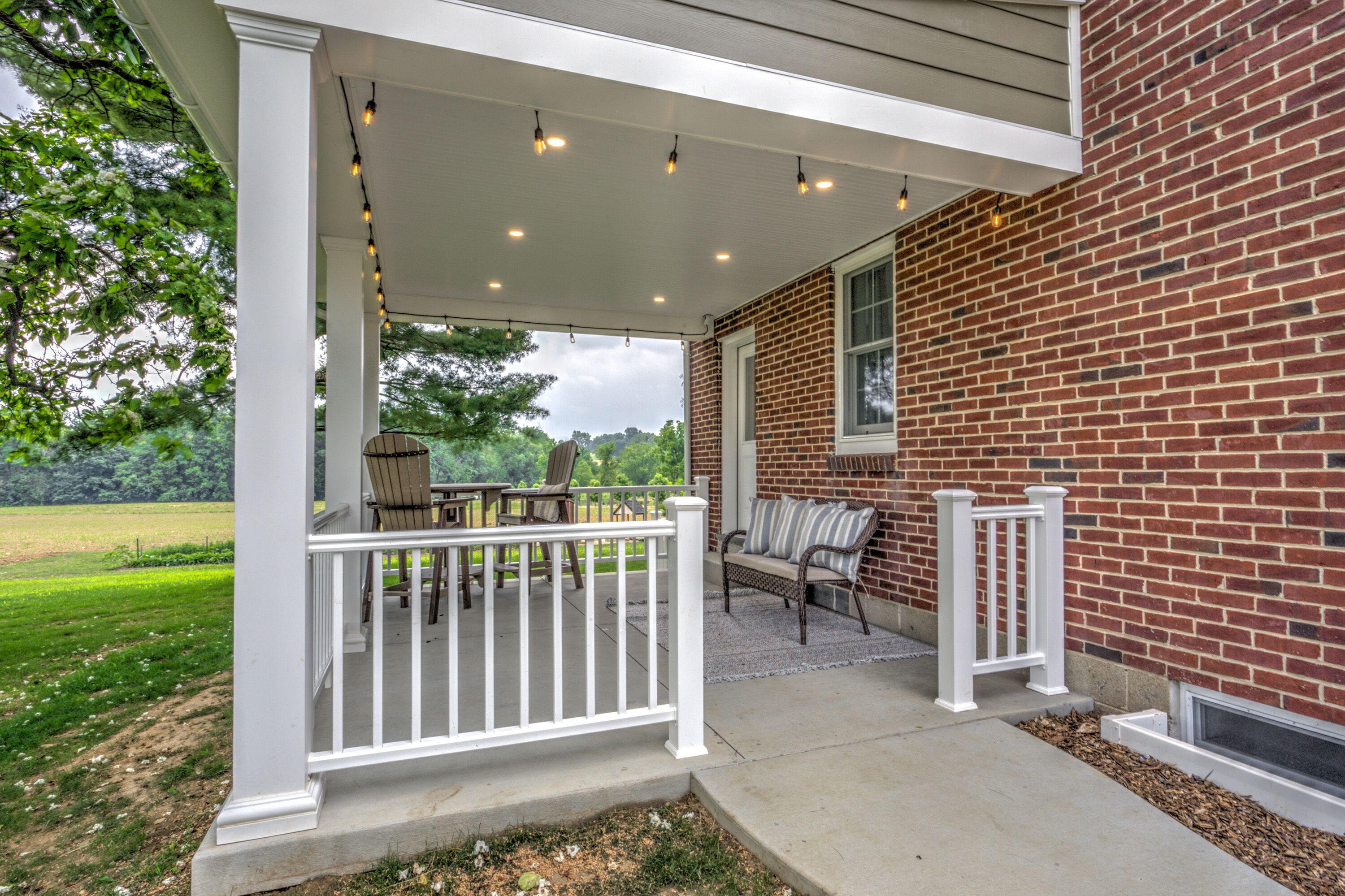 A covered porch with a brick wall, outdoor furniture, and string lights.