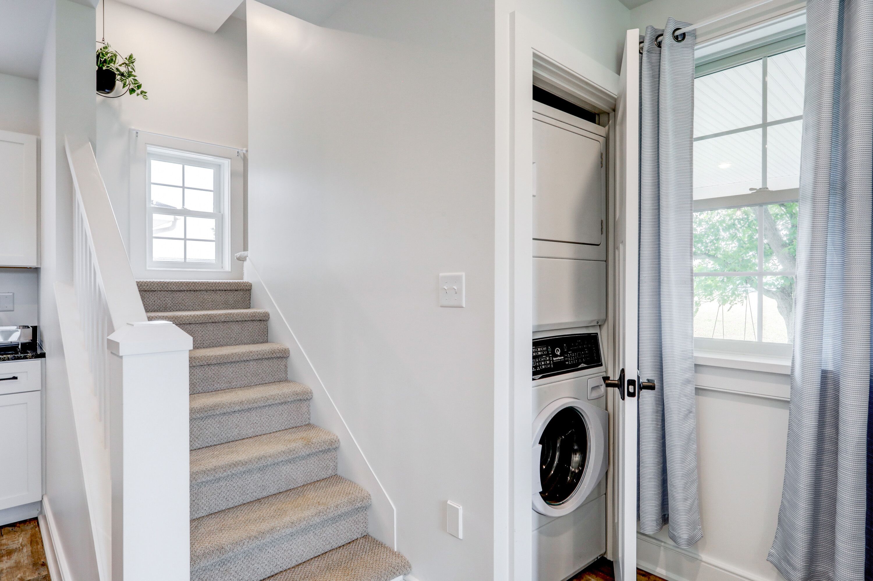 A laundry room with a washing machine, a dryer, and a window with curtains.