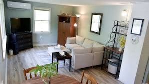 A living room with a sofa, a coffee table, a TV, and a dining table with chairs.