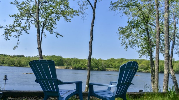 Two Adirondack chairs facing a lake with trees and a clear sky.