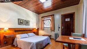 A hotel room with a wooden bed, a desk with a chair, a radiator, and a window with curtains. - Pousada Saint Gallen  (Campos do Jordão)