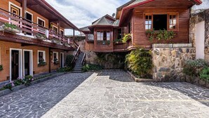 A traditional wooden building with a stone courtyard, featuring balconies with plants and a staircase leading to an upper level. - Pousada Saint Gallen  (Campos do Jordão)