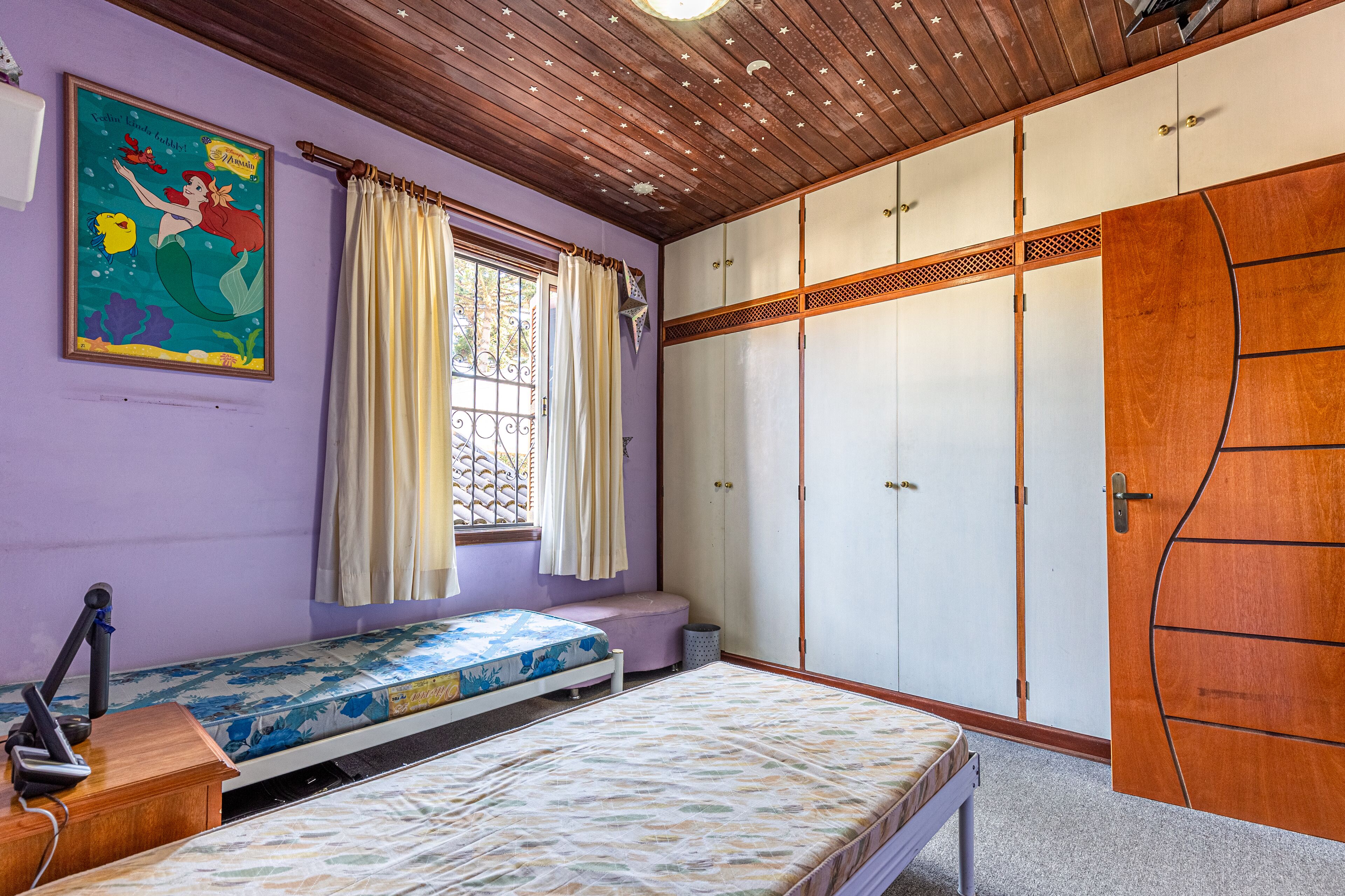 A bedroom with a bed, a window with curtains, a wardrobe, and a poster on the wall.
