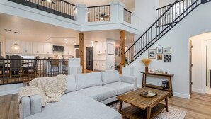 En rummelig opholdsstue med en stor grå hjørnesofa, et træbord og en trappe til en etage over.