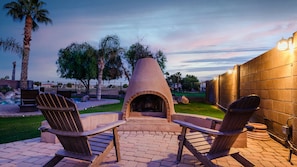 An outdoor patio with a stone fireplace, two Adirondack chairs, and a brick wall.
