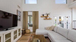 En moderne stue med et fladskærms-tv, en sofa, et sofabord og en tæppe med et mønster.