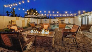 Un patio al aire libre con mobiliario de mimbre, un hogar para fuego y luces colgantes.