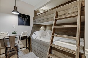 Un lit superposé avec une échelle, un bureau avec une chaise, une lampe suspendue et une plante fixée au mur.