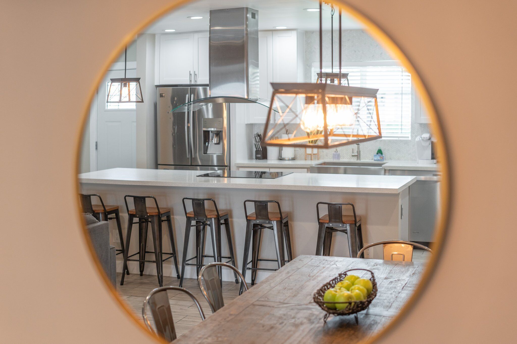 A modern kitchen with a central island, bar stools, and a dining table.