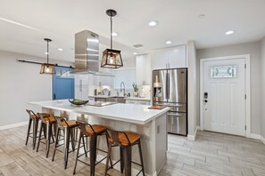 A modern kitchen with a large island, bar stools, stainless steel appliances, and pendant lighting. - Closest Walk to Old Town, Entertainment District (Scottsdale)