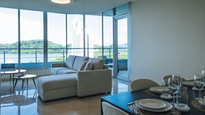 A modern room with a dining area, a sofa, and large windows offering a view of a building and greenery. - Apartment in Casa Bonita (Veracruz)
