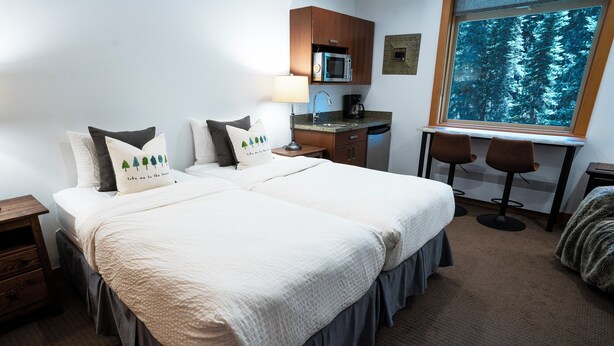 Ein Hotelzimmer mit Doppelbett, Schreibtisch, Mikrowelle, Kaffeemaschine und Fenster mit Blick auf den Wald.