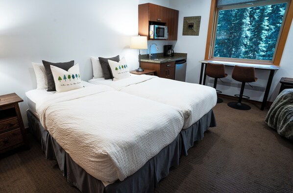 Une chambre d’hôtel avec un lit double, un bureau équipé d’un four à micro-ondes et d’une machine à café, ainsi qu’une fenêtre donnant sur la forêt.