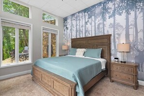 Un dormitorio con una cama grande, dos mesitas de noche y vistas al exterior a través de amplias ventanas.
