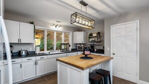 A kitchen with white cabinets, a wooden island, bar stools, a hanging light fixture, and a door. - Helen Lodge with Sauna and Hot Tub, 2 min to Helen (Helen)