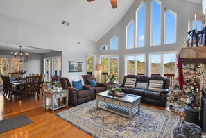 A spacious living room with a high ceiling, large windows, and a cozy fireplace.
