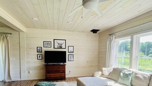 A living room with a sectional sofa, a flat-screen TV, wooden walls, and artwork. - Family Farmhouse (Watertown)