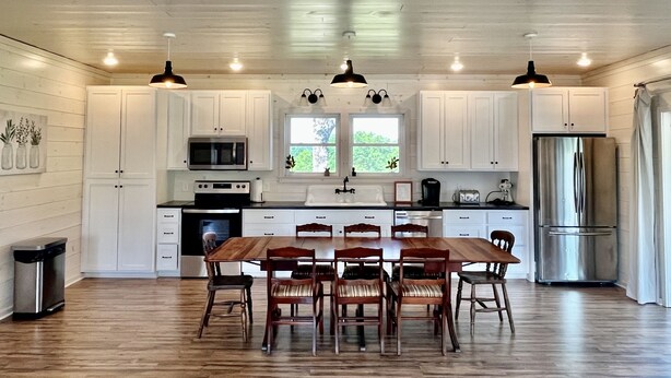 A modern kitchen with white cabinets, a wooden dining table, and a stainless steel refrigerator. - Family Farmhouse (Watertown)