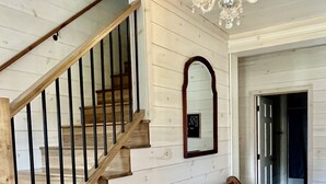 A wooden staircase with black railings, a bench with patterned cushions, and a chandelier. - Family Farmhouse (Watertown)