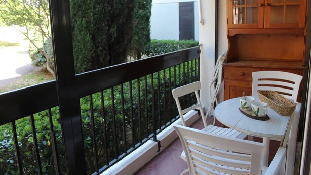 A balcony with a white chair and table, a wooden cabinet, and a view of greenery. - One-bedroom flat with terrace and parking space, 400 metres from the port - 4RS207 (SAINT CYPRIEN PLAGE)