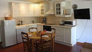 A compact kitchen with white cabinets, a dining table with chairs, a refrigerator, a coffee maker, a microwave, and a television mounted on the wall. - One-bedroom flat with terrace and parking space, 400 metres from the port - 4RS207 (SAINT CYPRIEN PLAGE)