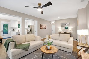Un salon moderne avec deux canapés, une table basse, un ventilateur de plafond et une cuisine en arrière-plan.