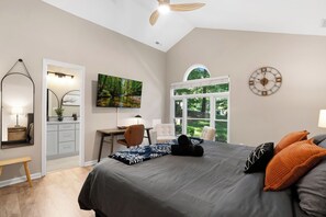 A bedroom with a bed, a desk, a chair, a window, and a clock on the wall.