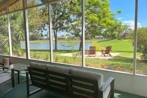 Una habitación con un amplio ventanal con vista a un lago y un espacio verde con dos sillas.
