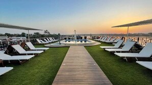 A rooftop lounge area with a wooden walkway leading to a central pool, surrounded by sun loungers and a clear view of the sunset. - Nile Cruise Aswoan & Luxor 3 & 4 Nights (Aswan)