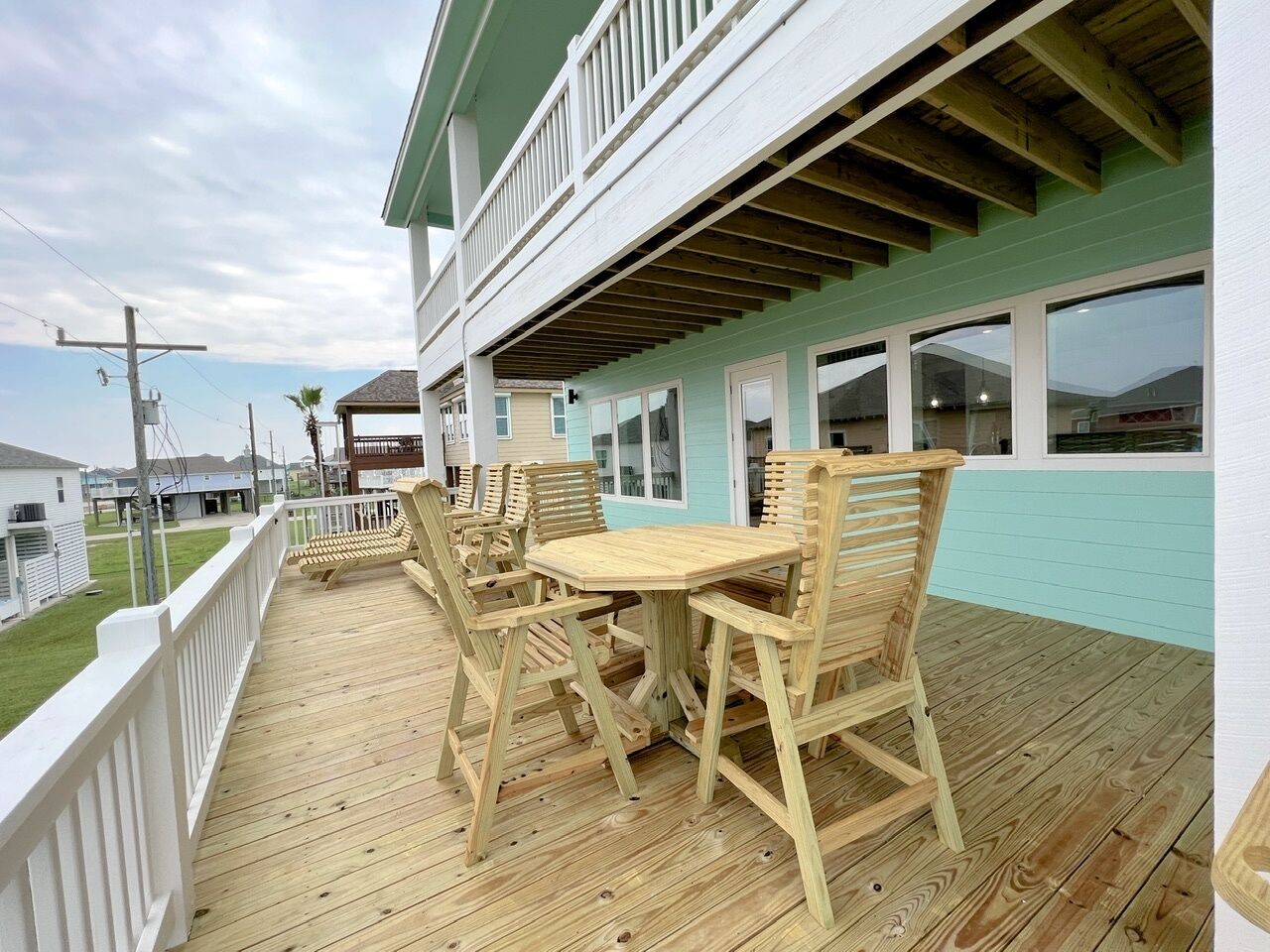A wooden deck with a table and chairs, a white railing, and a building with a green exterior and multiple windows.