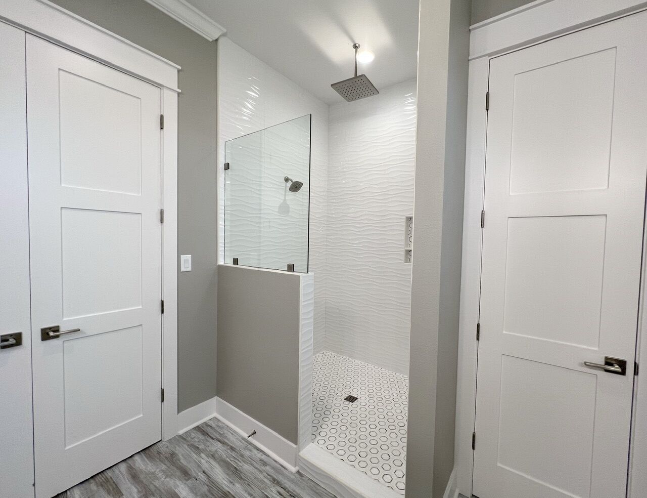 A bathroom with two white doors, a shower with a glass partition, and a patterned floor.