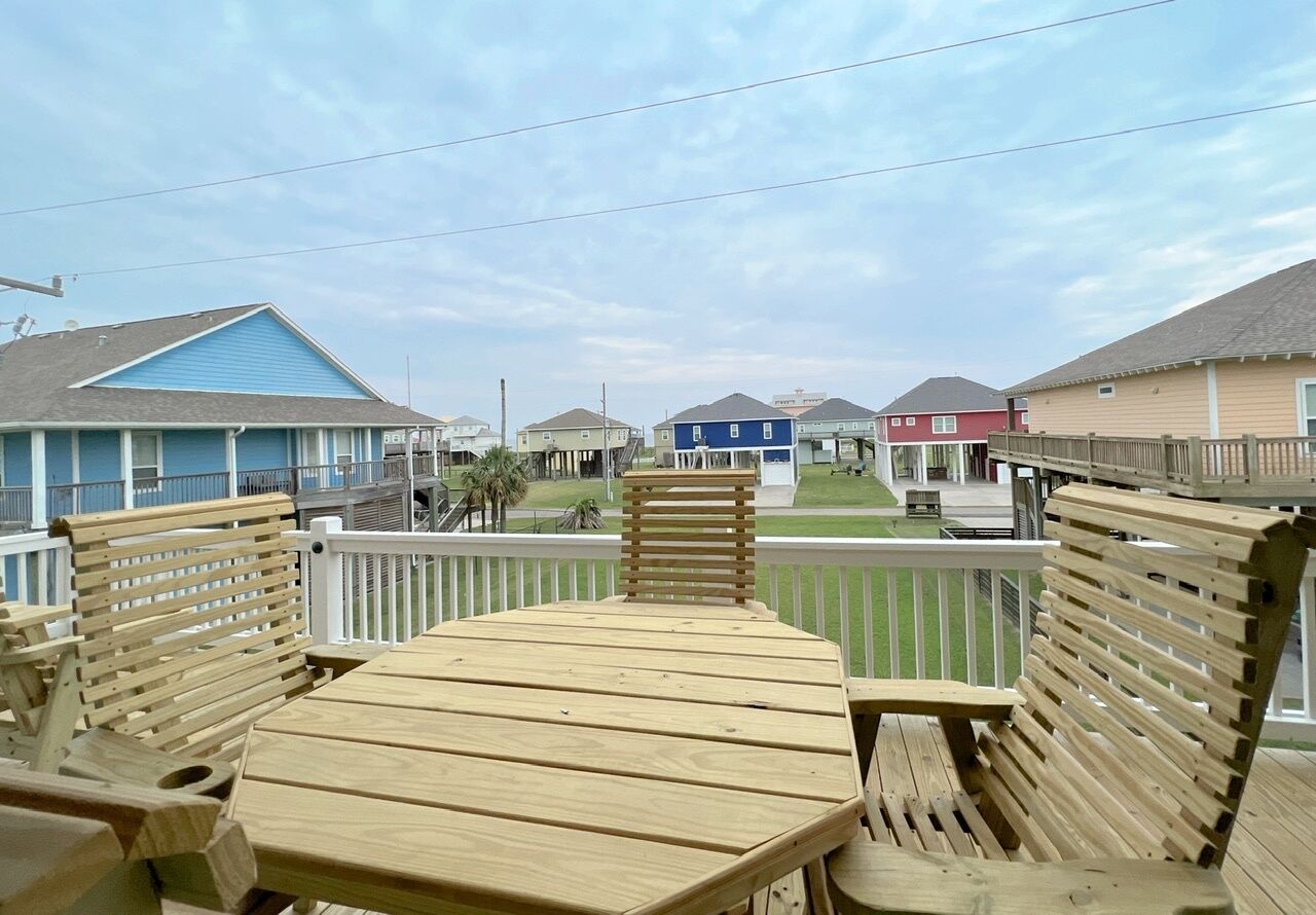 A wooden deck with a table and benches, overlooking a row of houses with a clear sky above.