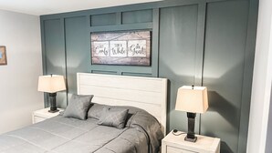 Une chambre à coucher comprenant un lit, deux tables de chevet avec des lampes, une tête de lit et une œuvre d’art accrochée au mur.