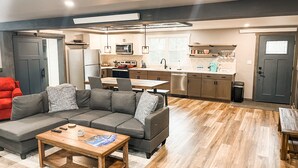Un salon moderne avec un canapé d’angle gris, une table basse en bois et un coin repas avec une cuisine en arrière-plan.